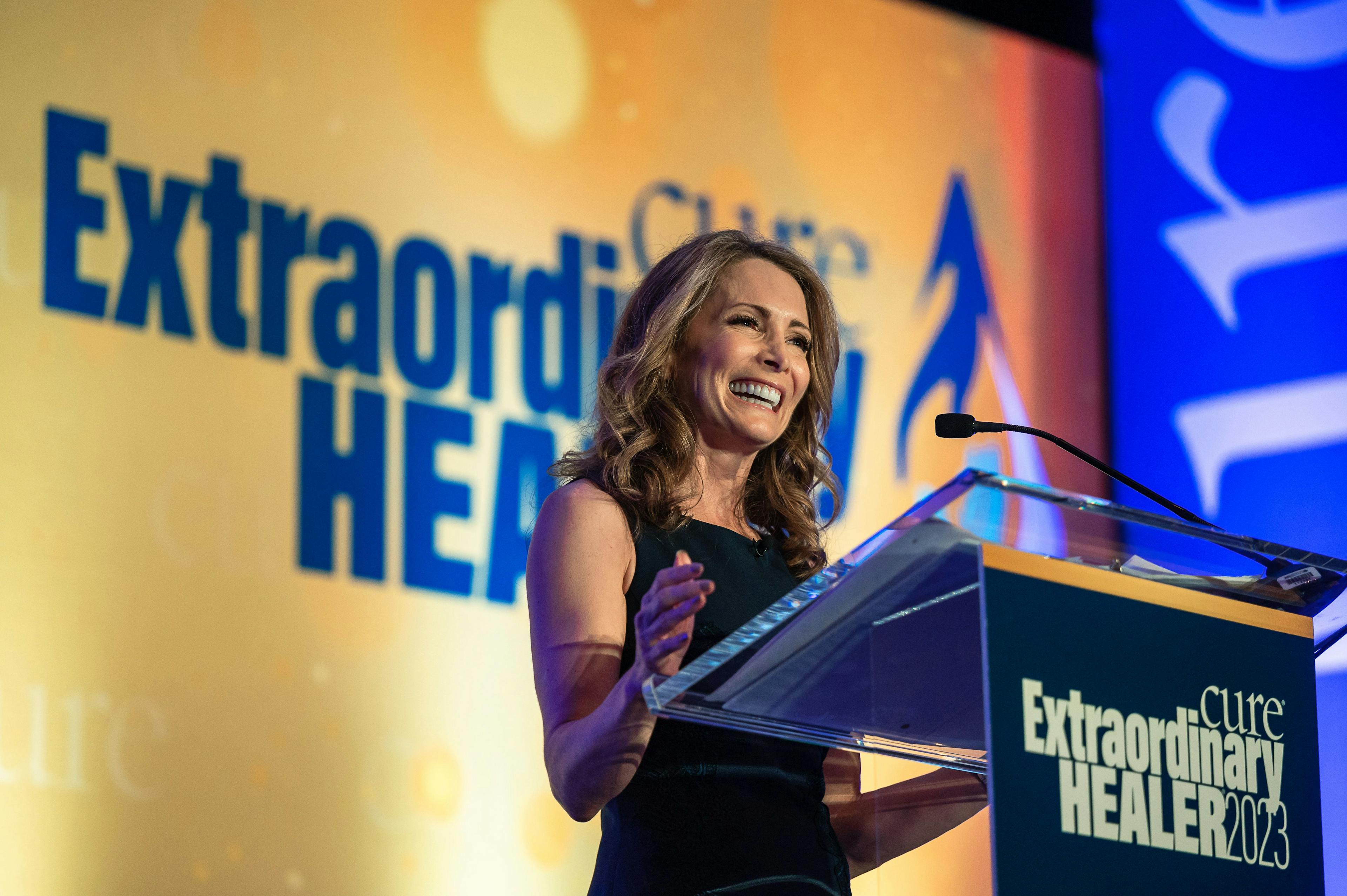 Shannon Miller smiling at a podium while delivering the keynote address at the 2023 Extraordinary Healer event | Image credit: © ATA-GIRL PHOTOGRAPHY