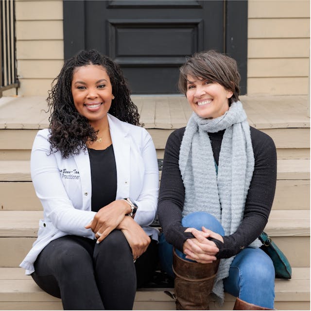 From left: Missy Bean-Tanner, RN, (a black nurse practitioner in a white labcoat) and Pamela Fields (a caucasian woman). Both are sitting on stairs outside, smiling at the camera. |  Photo by Sean Gasser