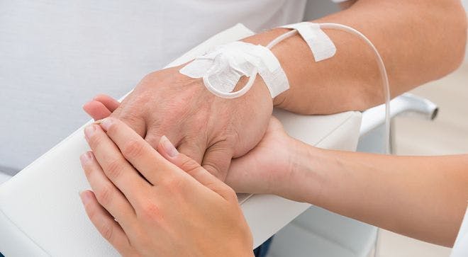 Image of a nurse holding the hand of a patient receiving chemotherapy.