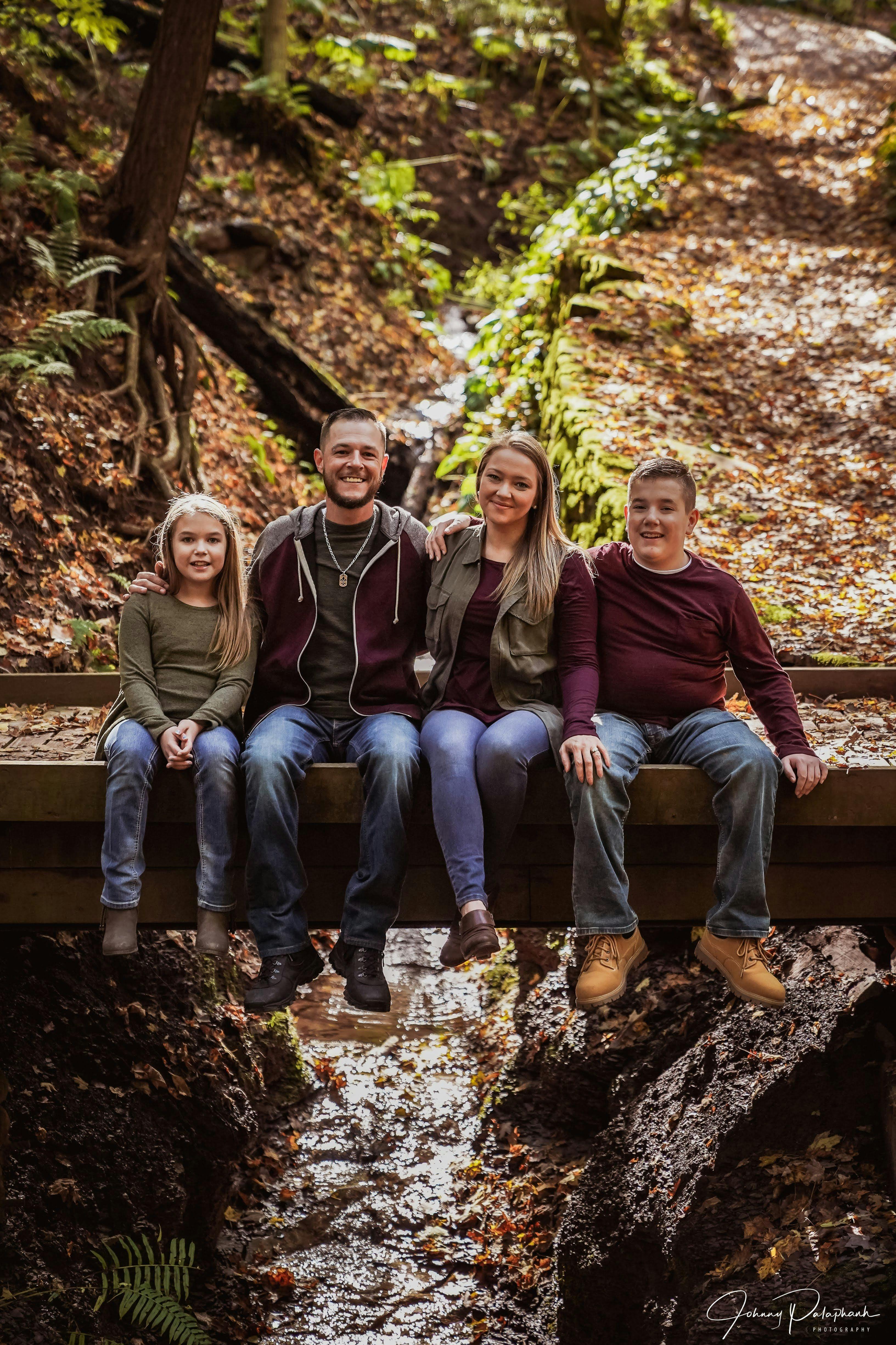 Photo of Amanda Brogna and her daughter, husband and son sitting on a bridge on a hiking trail